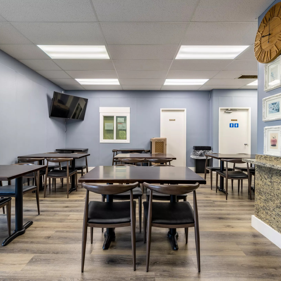 Empty dining room at Garlex Pizza & Ribs with dark tables and chairs, light blue walls, and wood floors.