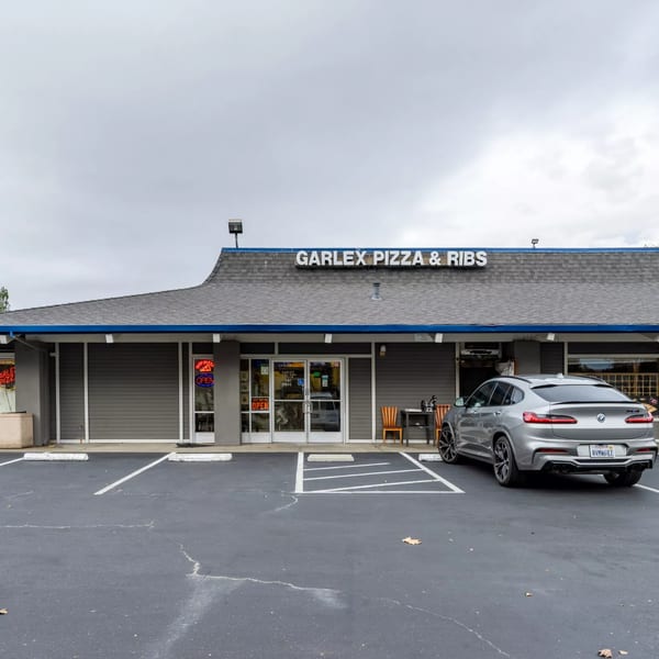 The exterior of Garlex Pizza & Ribs, a gray building with a blue-trimmed roof and a silver car parked outside.