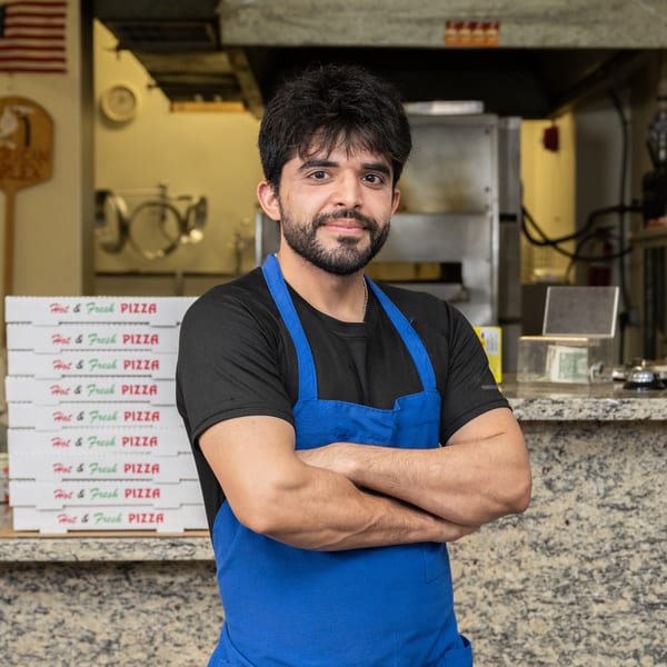 Garlex Pizza & Ribs employee in a blue apron standing in front of stacked pizza boxes.