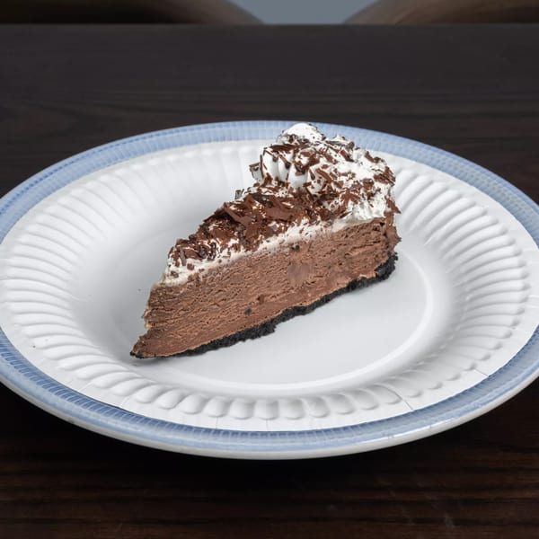 A slice of chocolate pie with whipped cream and chocolate shavings on a white plate.