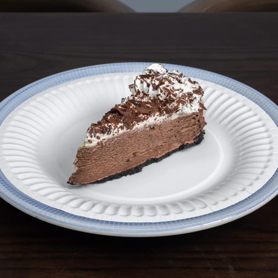 A slice of chocolate pie with whipped cream and chocolate shavings on a white plate.